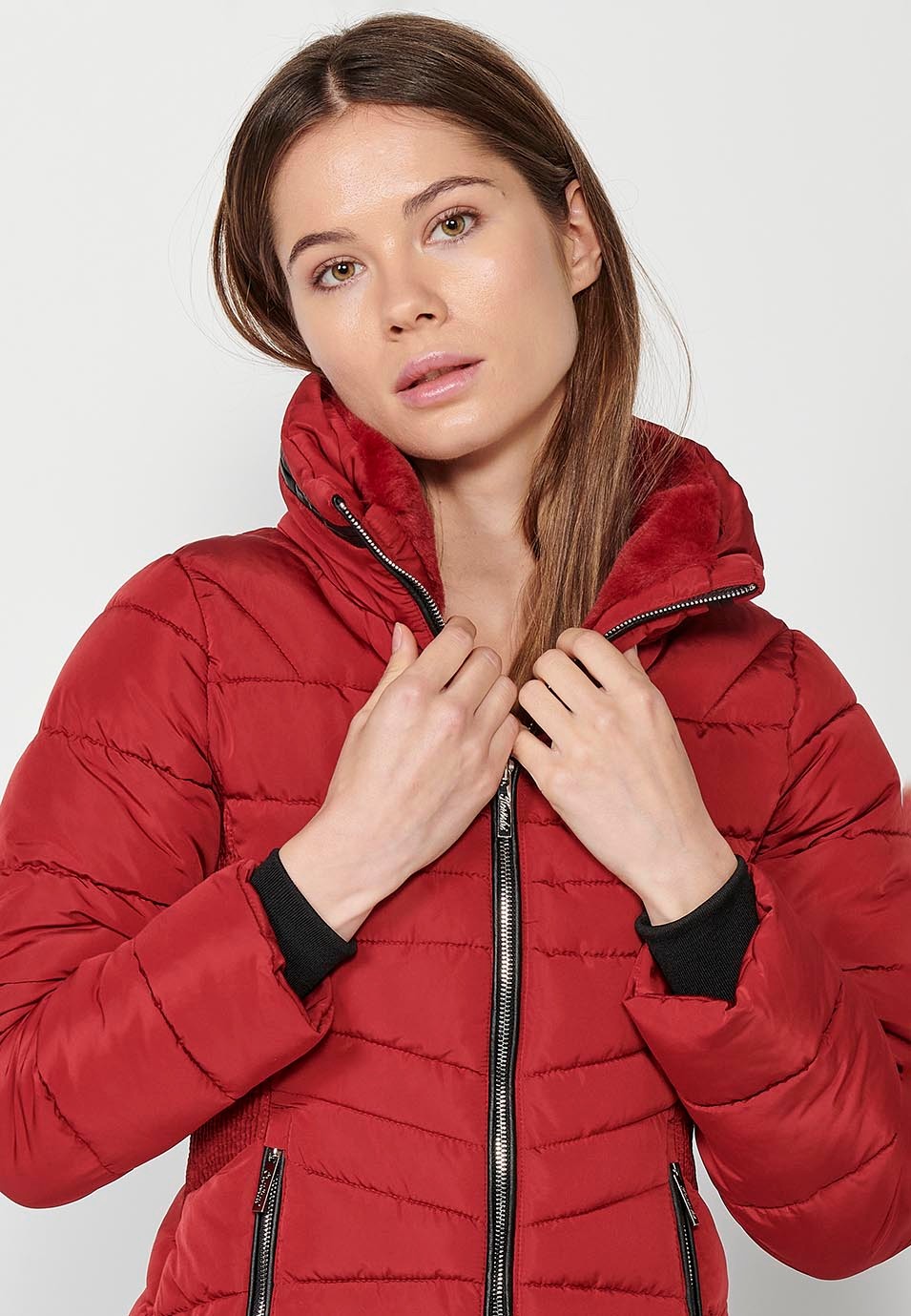 Parka courte rembourrée avec col montant et fermeture éclair sur le devant et poches rouges pour femme.