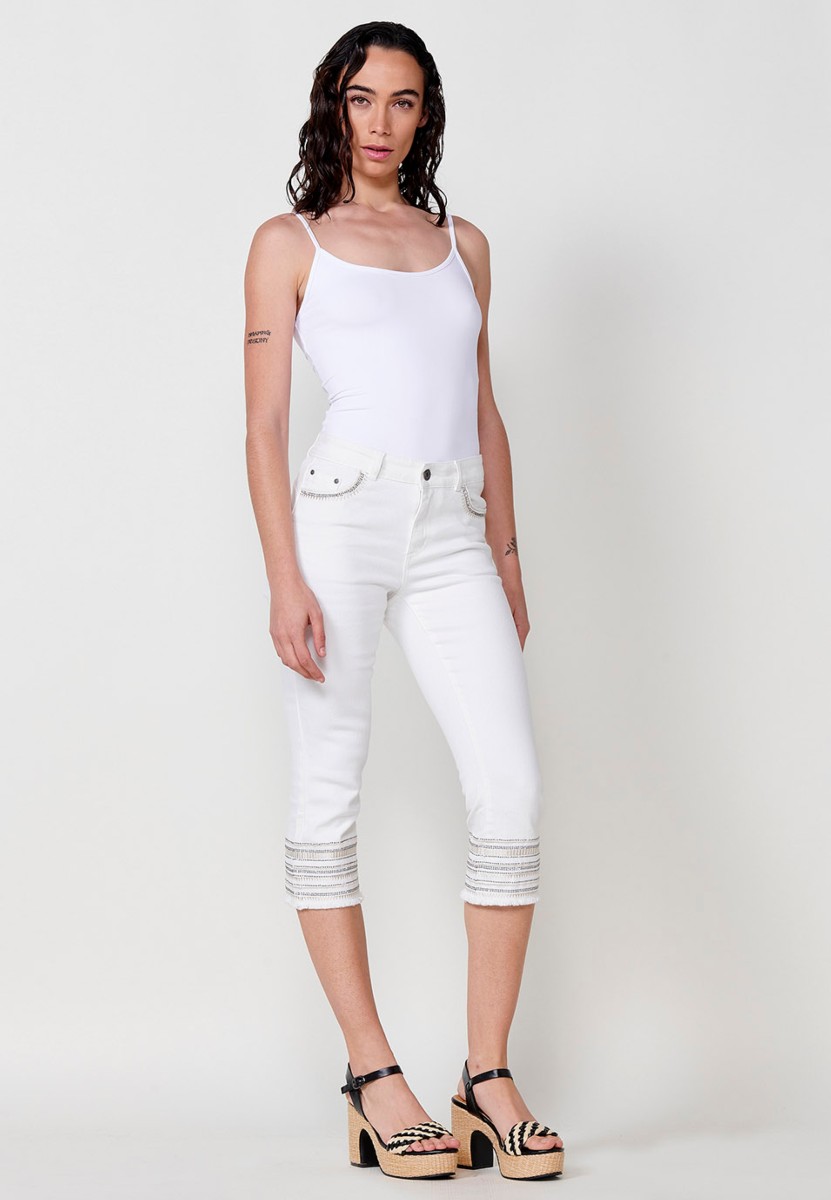 Pantalón jeans capri elástico push up tiro medio y cinco bolsillos con cierre con cremallera y botón metálico y bajo desilachado con bordado cenefa combinado con brillos para mujer de color blanco