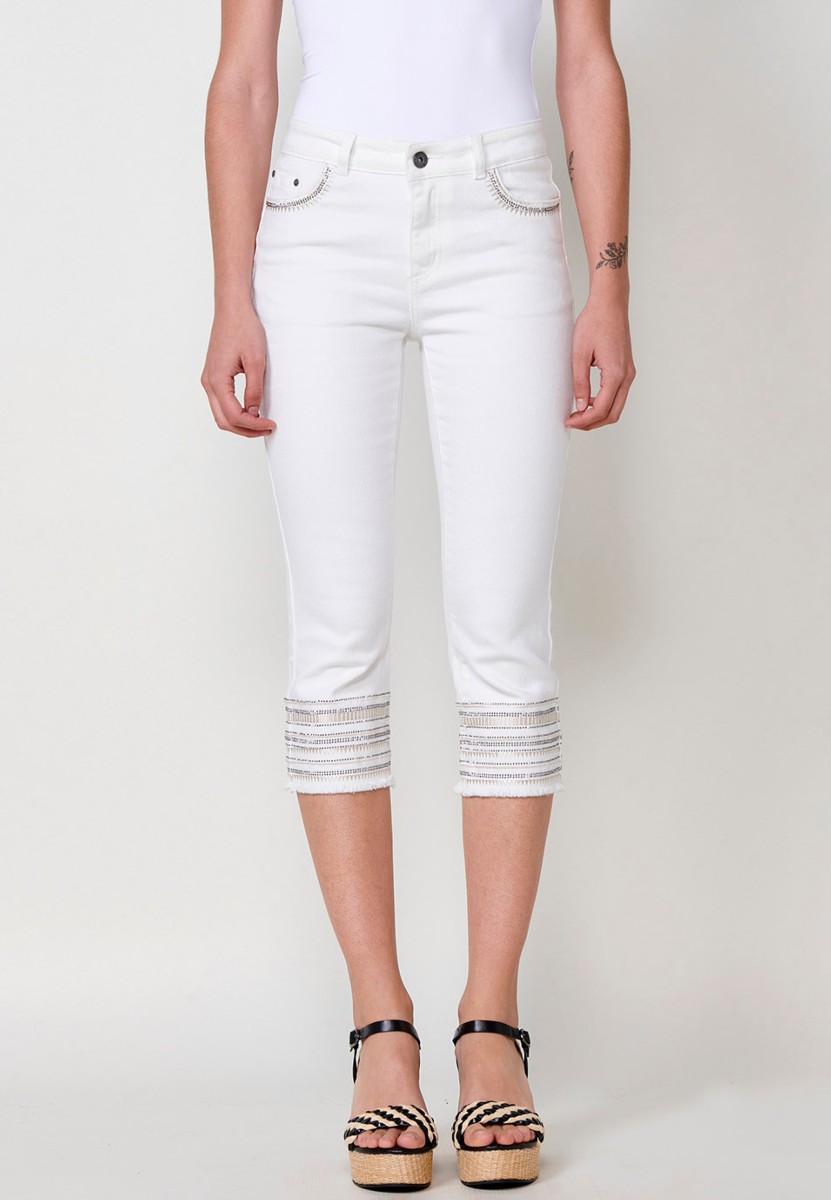 Pantalón jeans capri elástico push up tiro medio y cinco bolsillos con cierre con cremallera y botón metálico y bajo desilachado con bordado cenefa combinado con brillos para mujer de color blanco