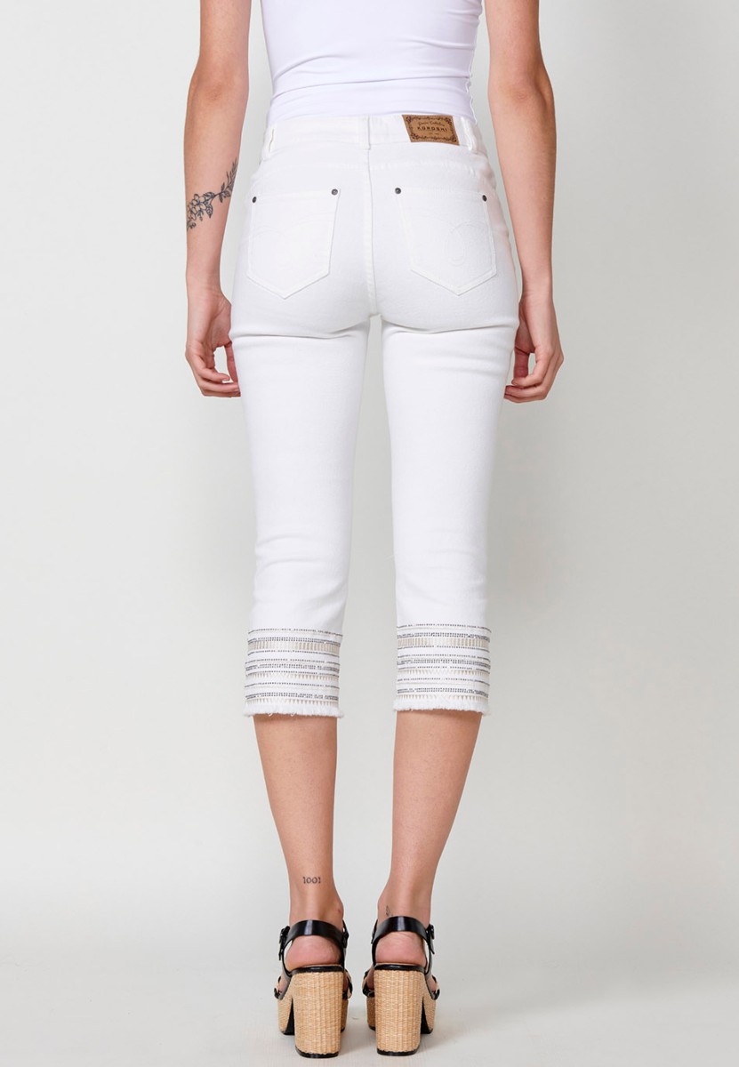 Pantalón jeans capri elástico push up tiro medio y cinco bolsillos con cierre con cremallera y botón metálico y bajo desilachado con bordado cenefa combinado con brillos para mujer de color blanco