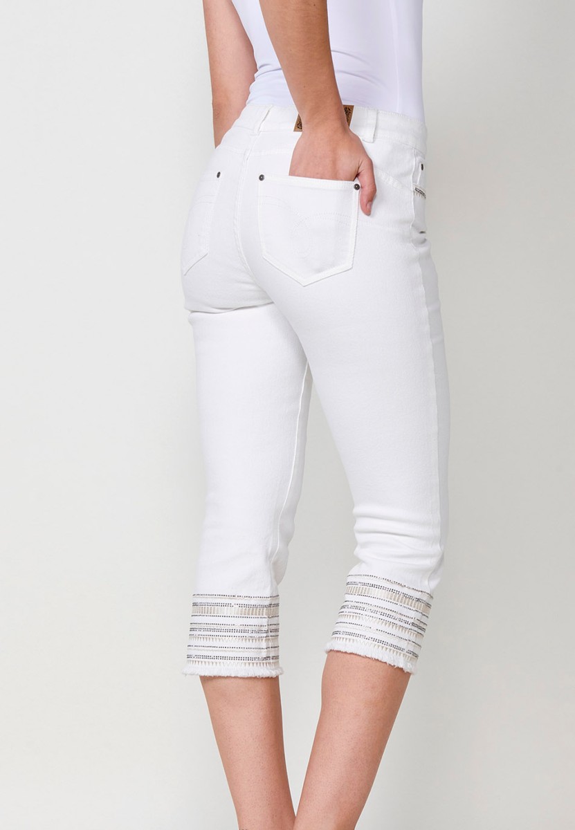 Pantalón jeans capri elástico push up tiro medio y cinco bolsillos con cierre con cremallera y botón metálico y bajo desilachado con bordado cenefa combinado con brillos para mujer de color blanco