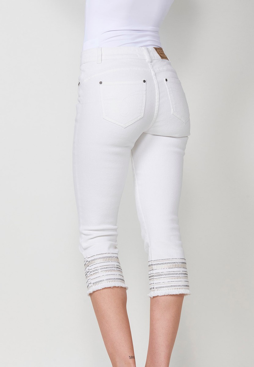 Pantalón jeans capri elástico push up tiro medio y cinco bolsillos con cierre con cremallera y botón metálico y bajo desilachado con bordado cenefa combinado con brillos para mujer de color blanco