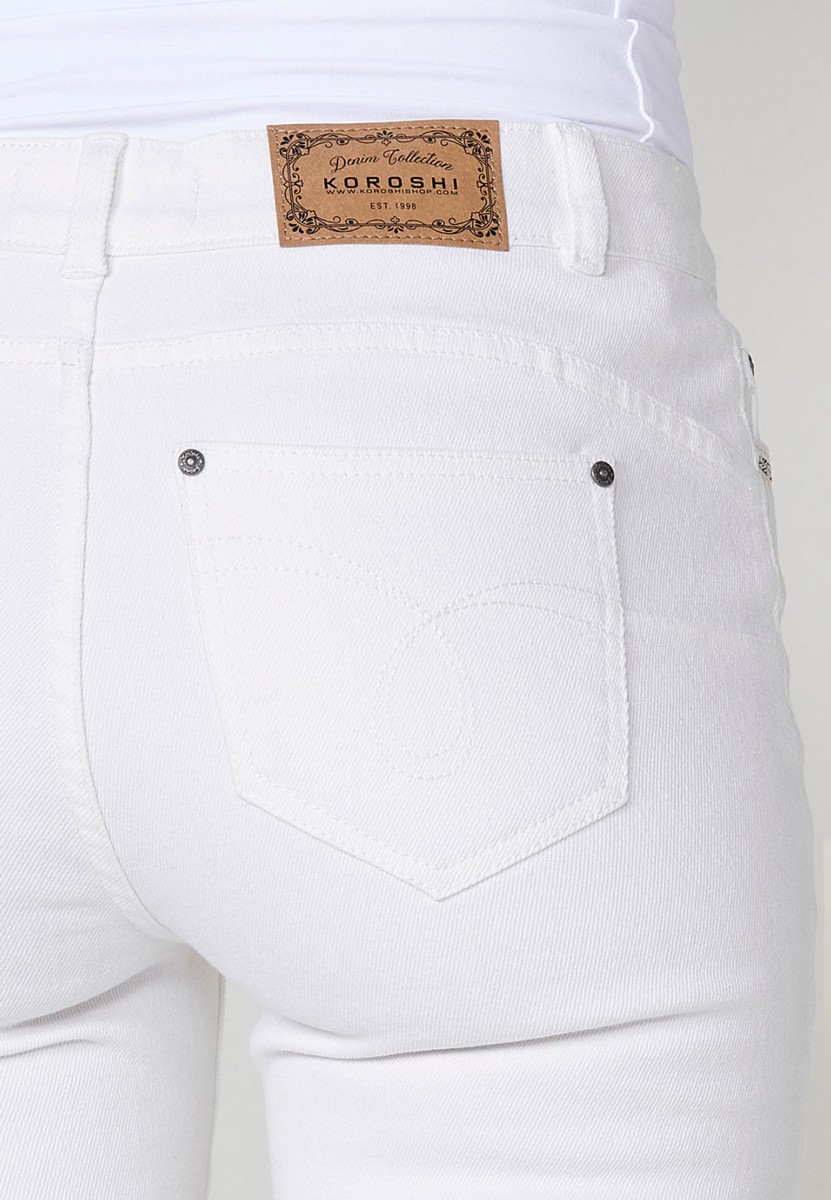 Pantalón jeans capri elástico push up tiro medio y cinco bolsillos con cierre con cremallera y botón metálico y bajo desilachado con bordado cenefa combinado con brillos para mujer de color blanco