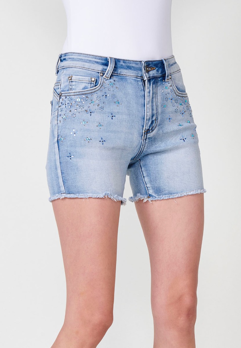 Jeans short elástico push up de tiro medio y cinco bolsillos con cierre y cremallera y botón metálico con detalle de brillos en bolsillos y bajo deshilachado para mujer de color azul claro