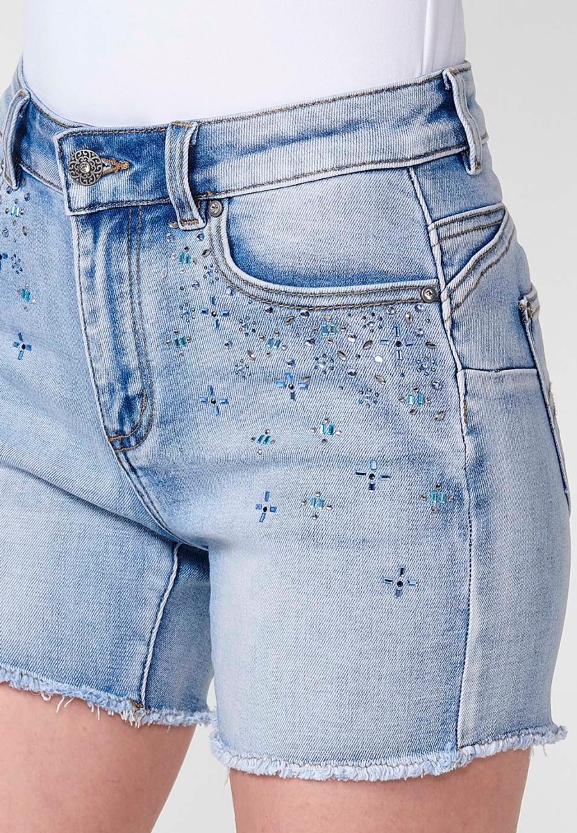 Jeans short elástico push up de tiro medio y cinco bolsillos con cierre y cremallera y botón metálico con detalle de brillos en bolsillos y bajo deshilachado para mujer de color azul claro