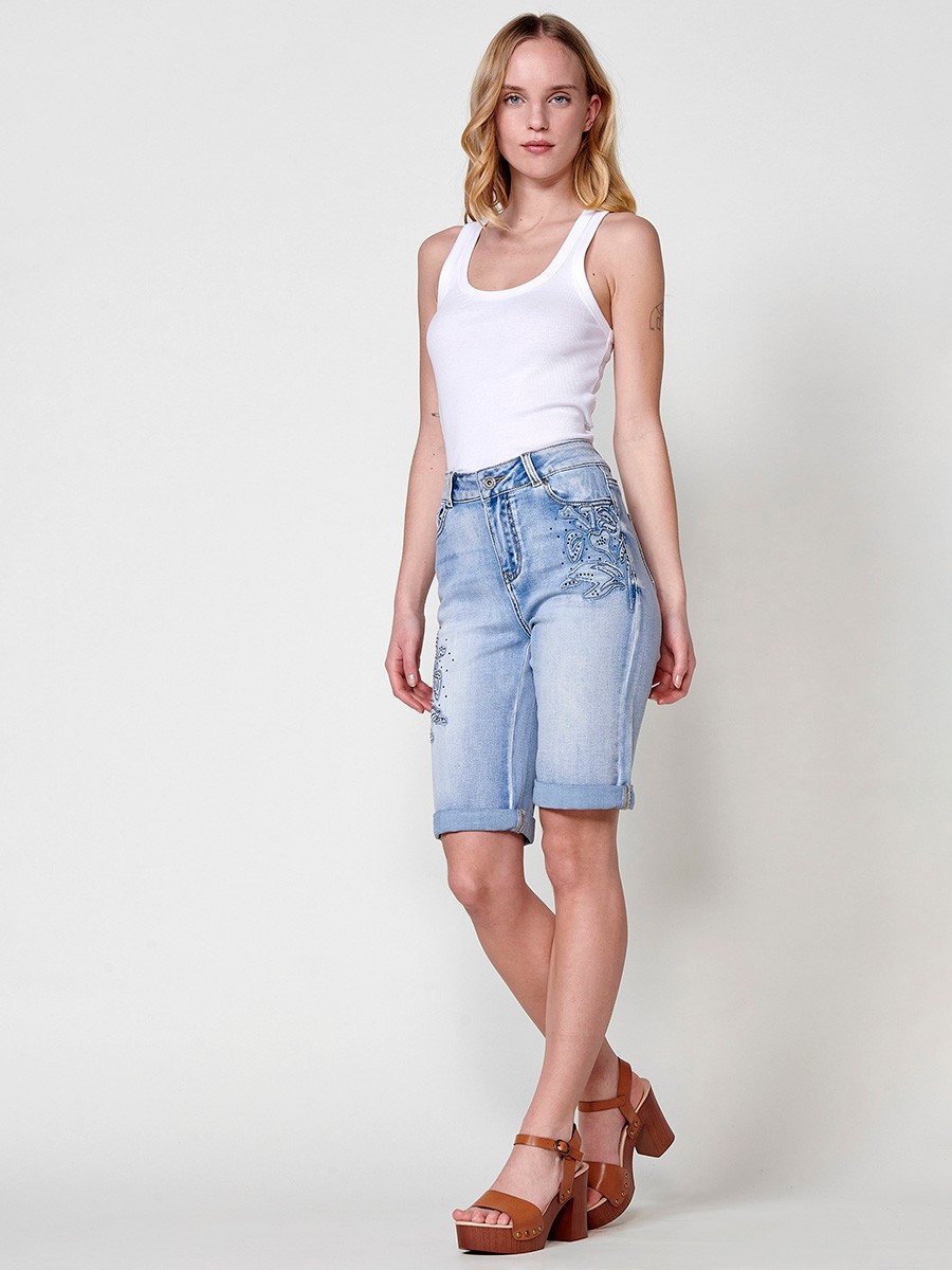 Jeans short elástico color lavado azul claro de Tiro medio y cinco bolsillos con Cierre con cremallera y botón metálico tiene el Bajo con doble vuelta y Patch de tejidos bordado y deshilachado con brillos para Mujer