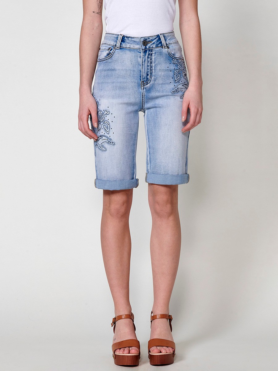 Jeans short elástico color lavado azul claro de Tiro medio y cinco bolsillos con Cierre con cremallera y botón metálico tiene el Bajo con doble vuelta y Patch de tejidos bordado y deshilachado con brillos para Mujer