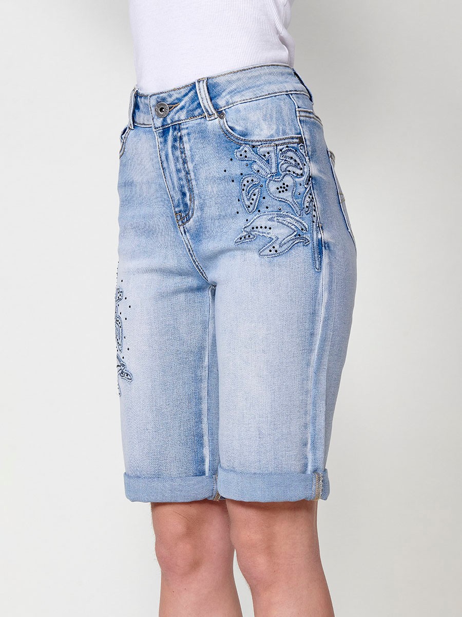 Jeans short elástico color lavado azul claro de Tiro medio y cinco bolsillos con Cierre con cremallera y botón metálico tiene el Bajo con doble vuelta y Patch de tejidos bordado y deshilachado con brillos para Mujer