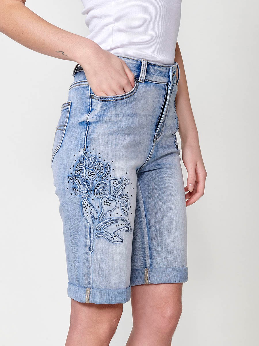 Jeans short elástico color lavado azul claro de Tiro medio y cinco bolsillos con Cierre con cremallera y botón metálico tiene el Bajo con doble vuelta y Patch de tejidos bordado y deshilachado con brillos para Mujer