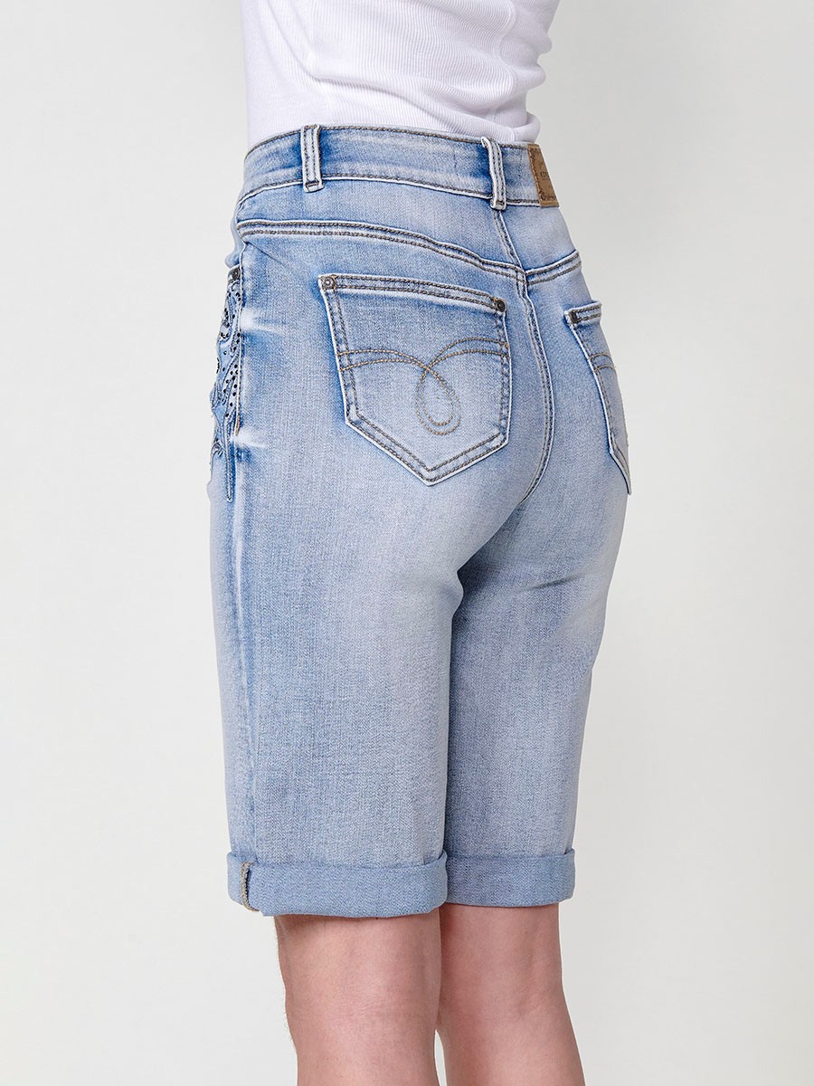 Jeans short elástico color lavado azul claro de Tiro medio y cinco bolsillos con Cierre con cremallera y botón metálico tiene el Bajo con doble vuelta y Patch de tejidos bordado y deshilachado con brillos para Mujer