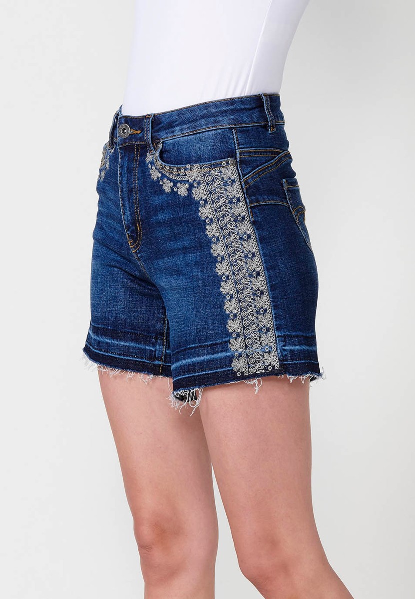 Jeans short elástico cenefa bordada en bolsillo y lateral de tiro medio y cinco bolsillos con cierre con cremallera y botón metálico y bajo deshilachado para mujer de color azul oscuro