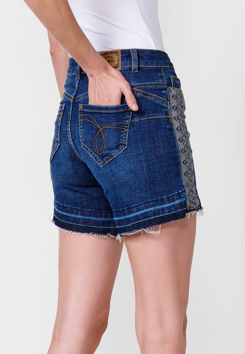 Jeans short elástico cenefa bordada en bolsillo y lateral de tiro medio y cinco bolsillos con cierre con cremallera y botón metálico y bajo deshilachado para mujer de color azul oscuro