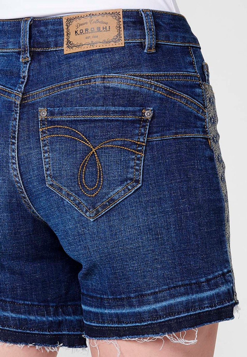 Jeans short elástico cenefa bordada en bolsillo y lateral de tiro medio y cinco bolsillos con cierre con cremallera y botón metálico y bajo deshilachado para mujer de color azul oscuro