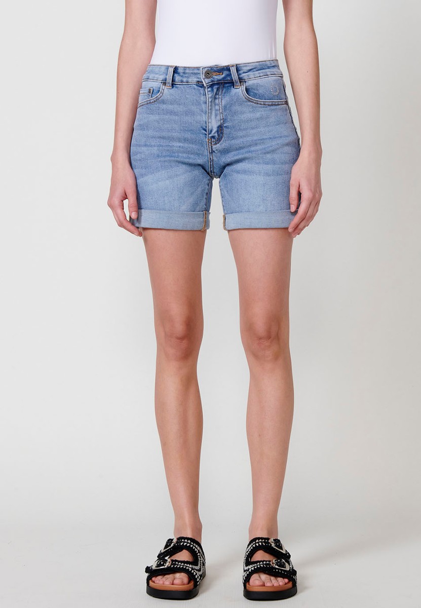 Jeans short elástico de tiro medio y cinco bolsillos con cierre con cremallera y botón metálico con bajo doble vuelta y logo con brillos para mujer de color azul claro