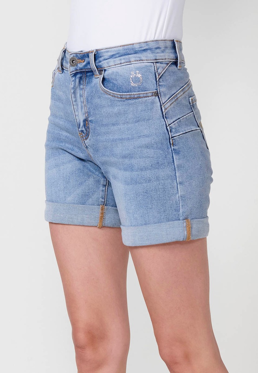 Jeans short elástico de tiro medio y cinco bolsillos con cierre con cremallera y botón metálico con bajo doble vuelta y logo con brillos para mujer de color azul claro