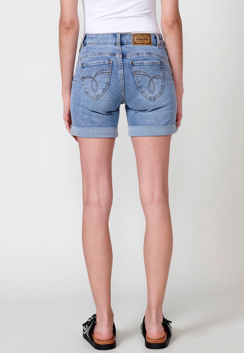 Jeans short elástico de tiro medio y cinco bolsillos con cierre con cremallera y botón metálico con bajo doble vuelta y logo con brillos para mujer de color azul claro