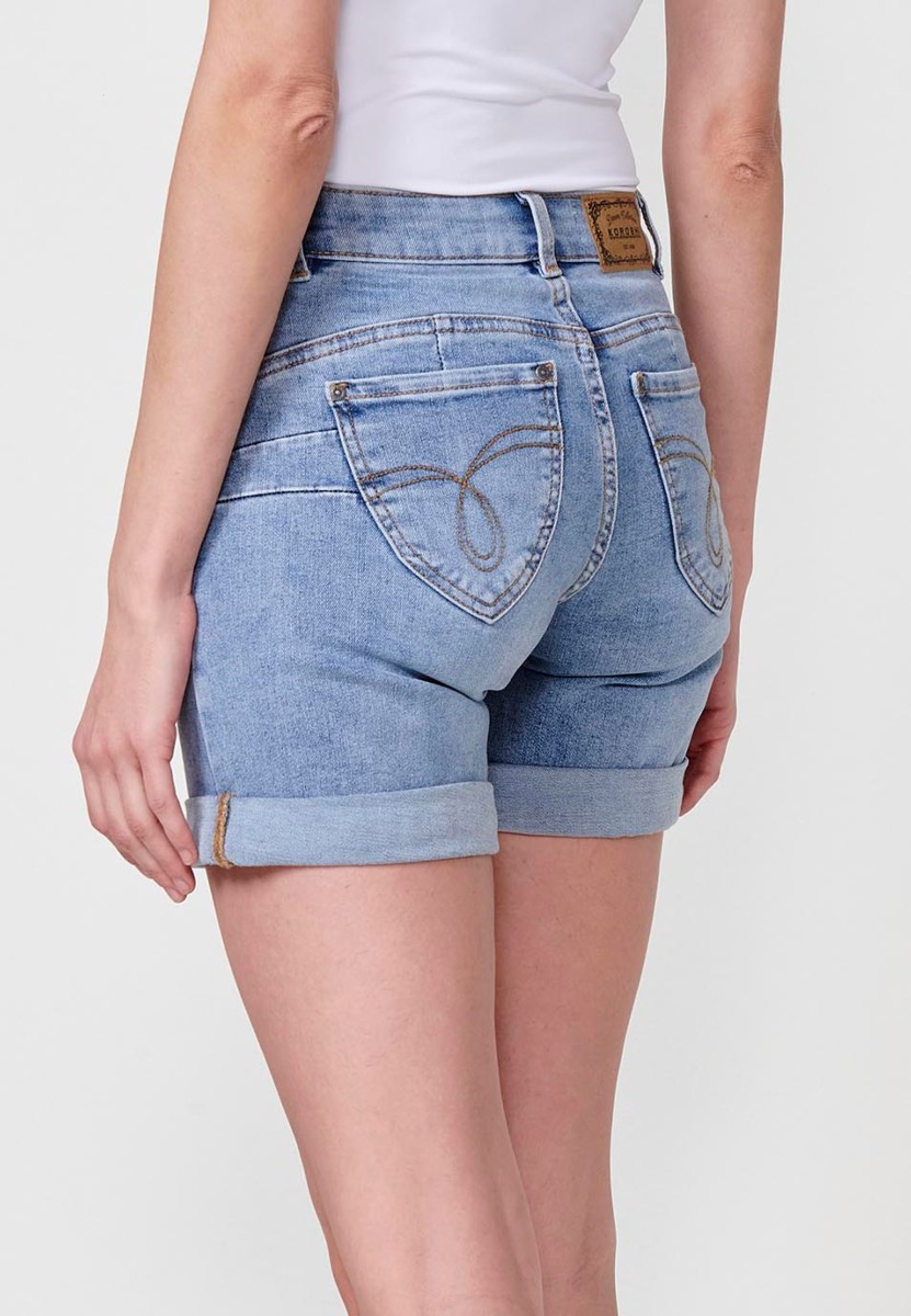 Jeans short elástico de tiro medio y cinco bolsillos con cierre con cremallera y botón metálico con bajo doble vuelta y logo con brillos para mujer de color azul claro