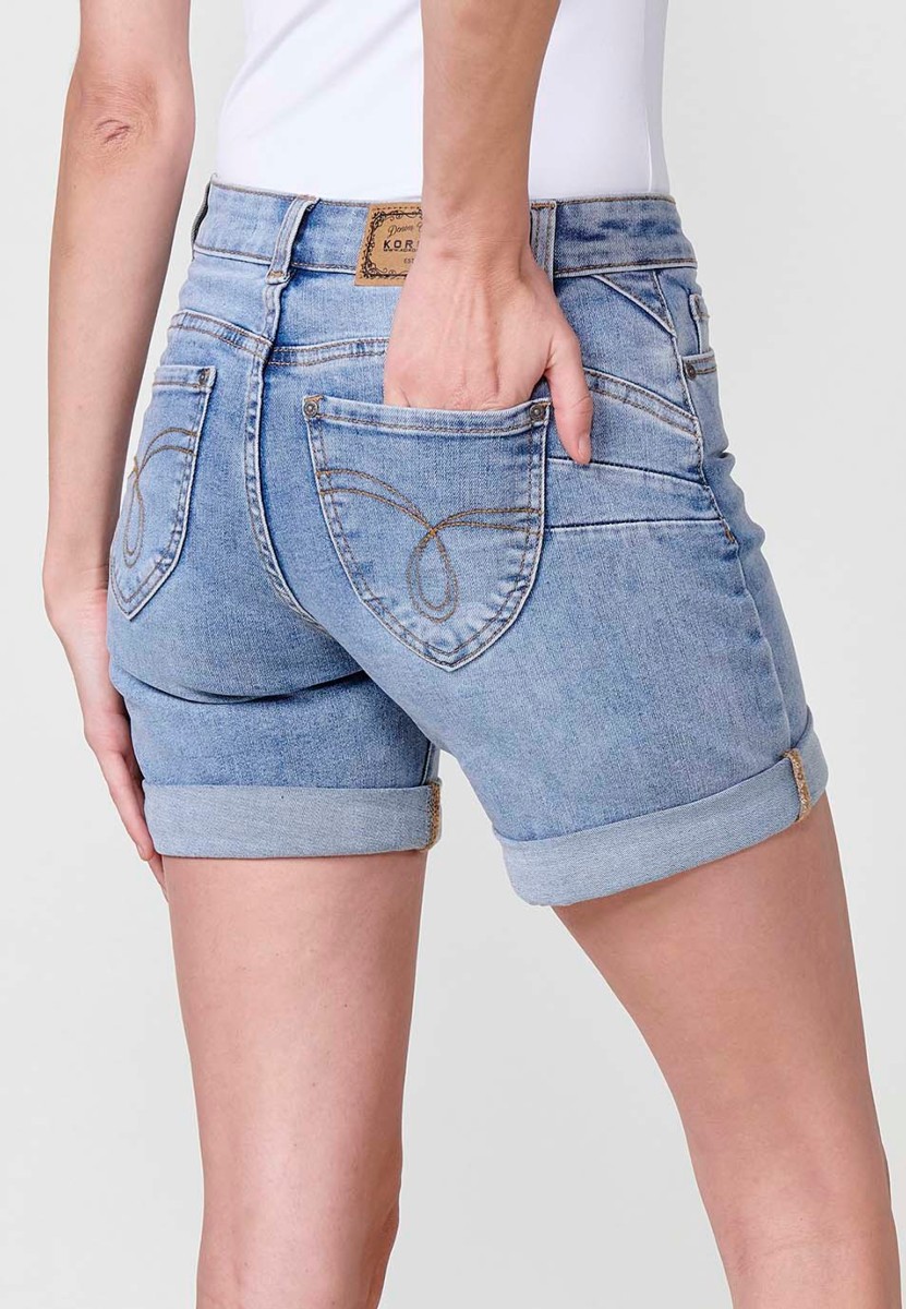 Jeans short elástico de tiro medio y cinco bolsillos con cierre con cremallera y botón metálico con bajo doble vuelta y logo con brillos para mujer de color azul claro