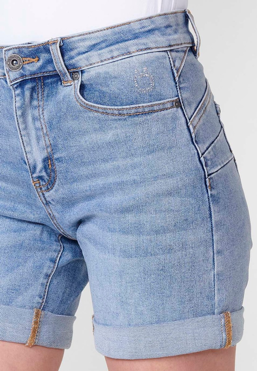 Jeans short elástico de tiro medio y cinco bolsillos con cierre con cremallera y botón metálico con bajo doble vuelta y logo con brillos para mujer de color azul claro