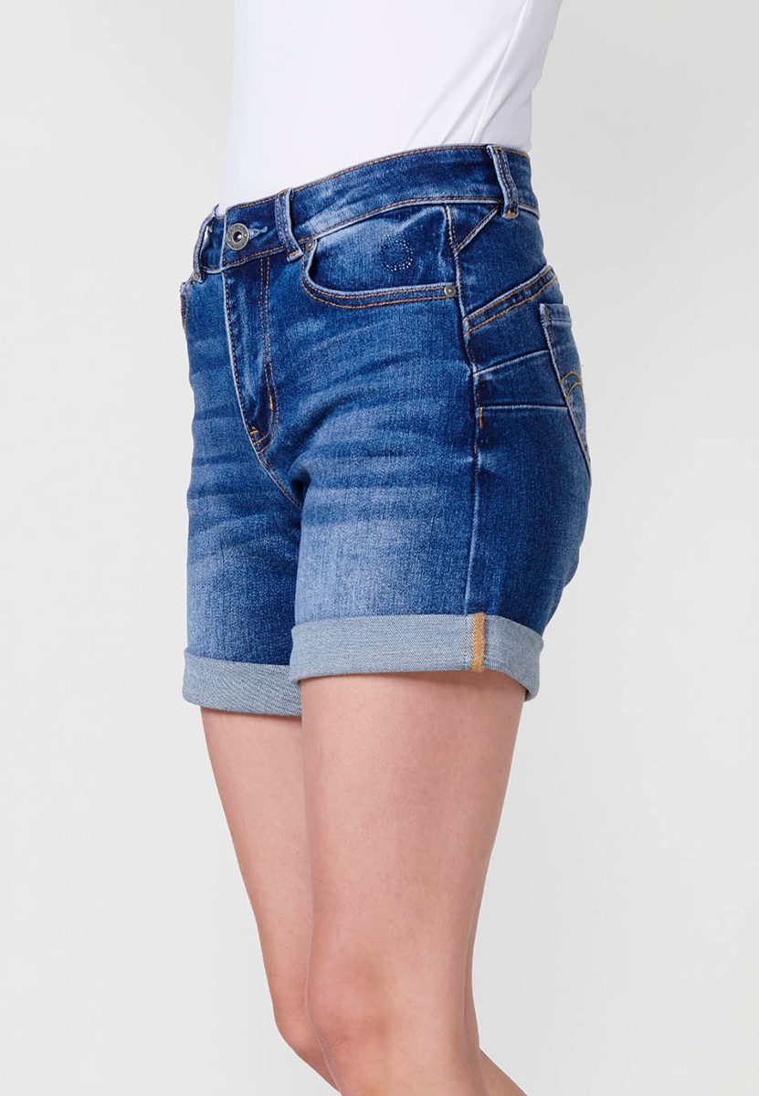 Jeans short elástico de tiro medio y cinco bolsillos con cierre con cremallera y botón metálico con bajo doble vuelta y logo con brillos para mujer de color azul oscuro