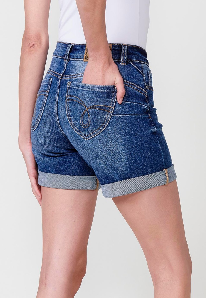 Jeans short elástico de tiro medio y cinco bolsillos con cierre con cremallera y botón metálico con bajo doble vuelta y logo con brillos para mujer de color azul oscuro