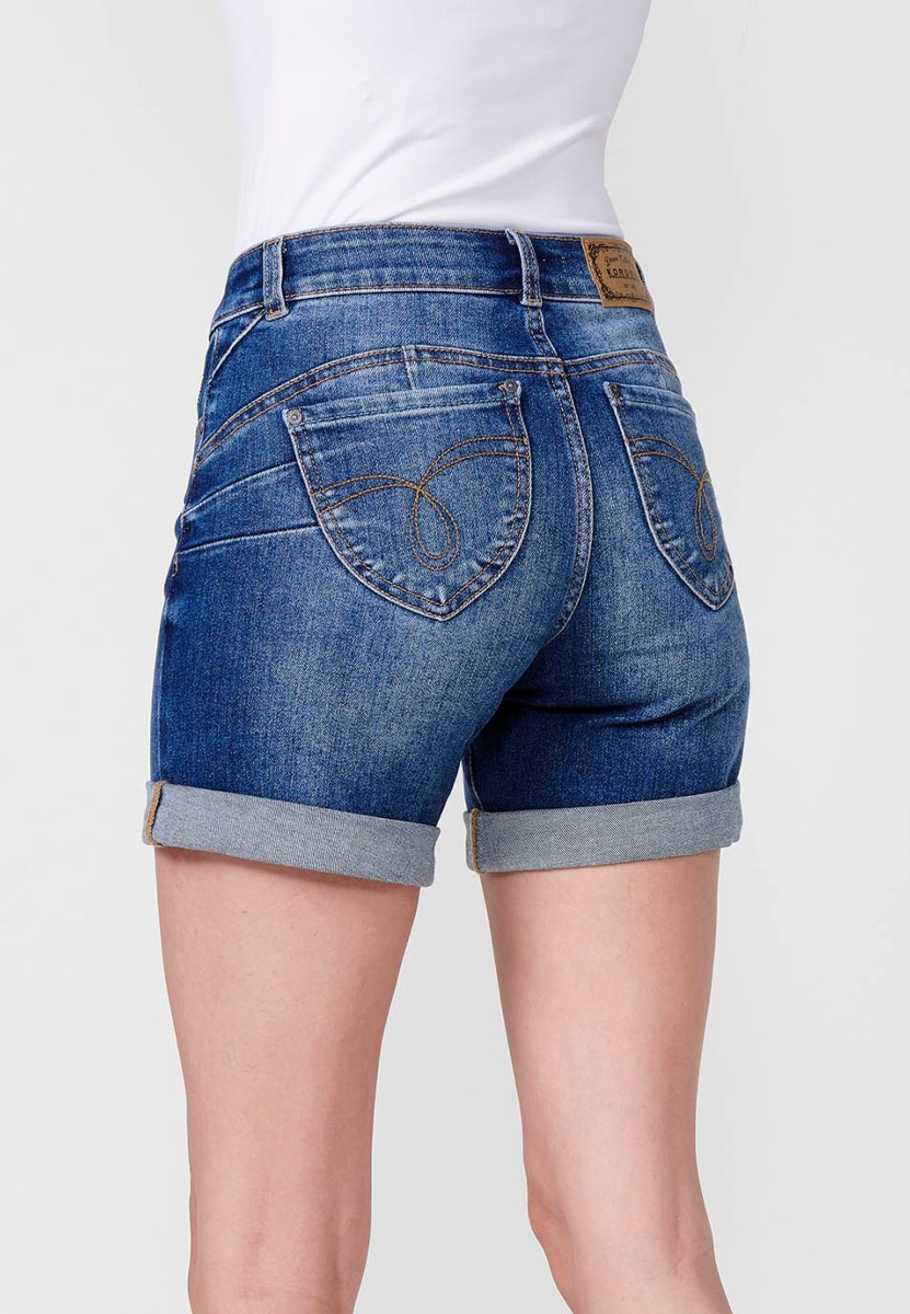 Jeans short elástico de tiro medio y cinco bolsillos con cierre con cremallera y botón metálico con bajo doble vuelta y logo con brillos para mujer de color azul oscuro